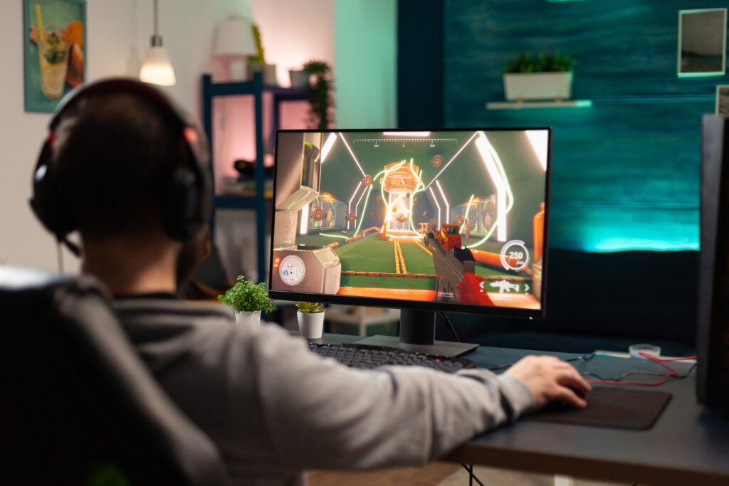 Adult playing video games on monitor with mouse and headphones. Gamer using mousepad and headset to play online games on computer. Player having fun with gaming and electronic game