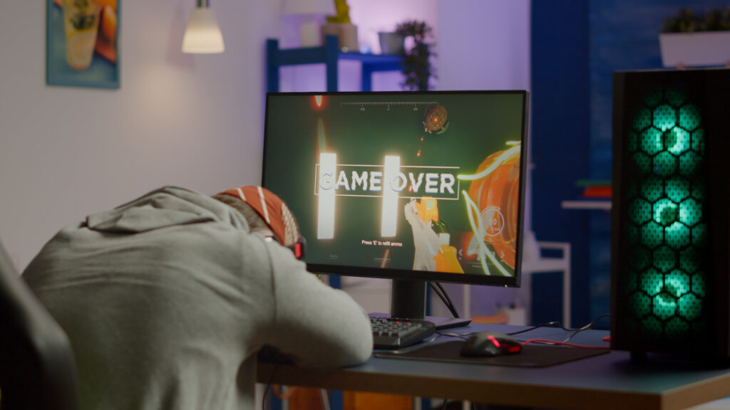 Game over for sad gamer playing shooter video games on powerful computer using RGB keyboard in gaming room.