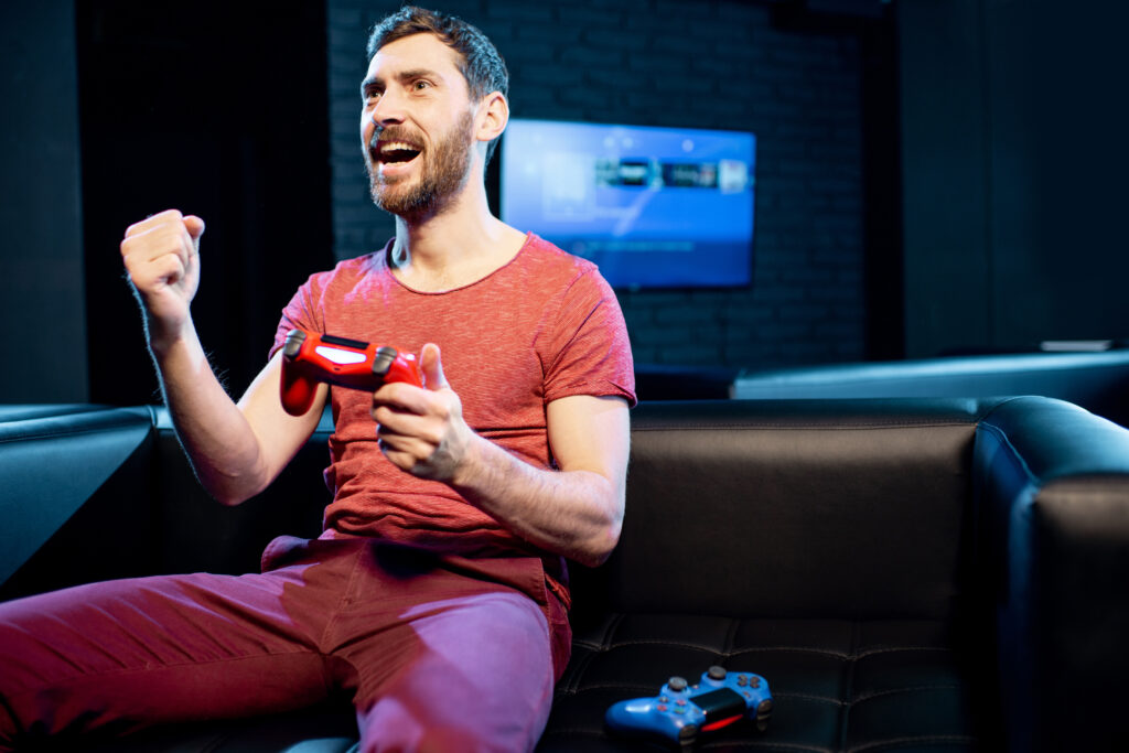 Happy man winning in video game playing with gaming console on the couch in a dark room.