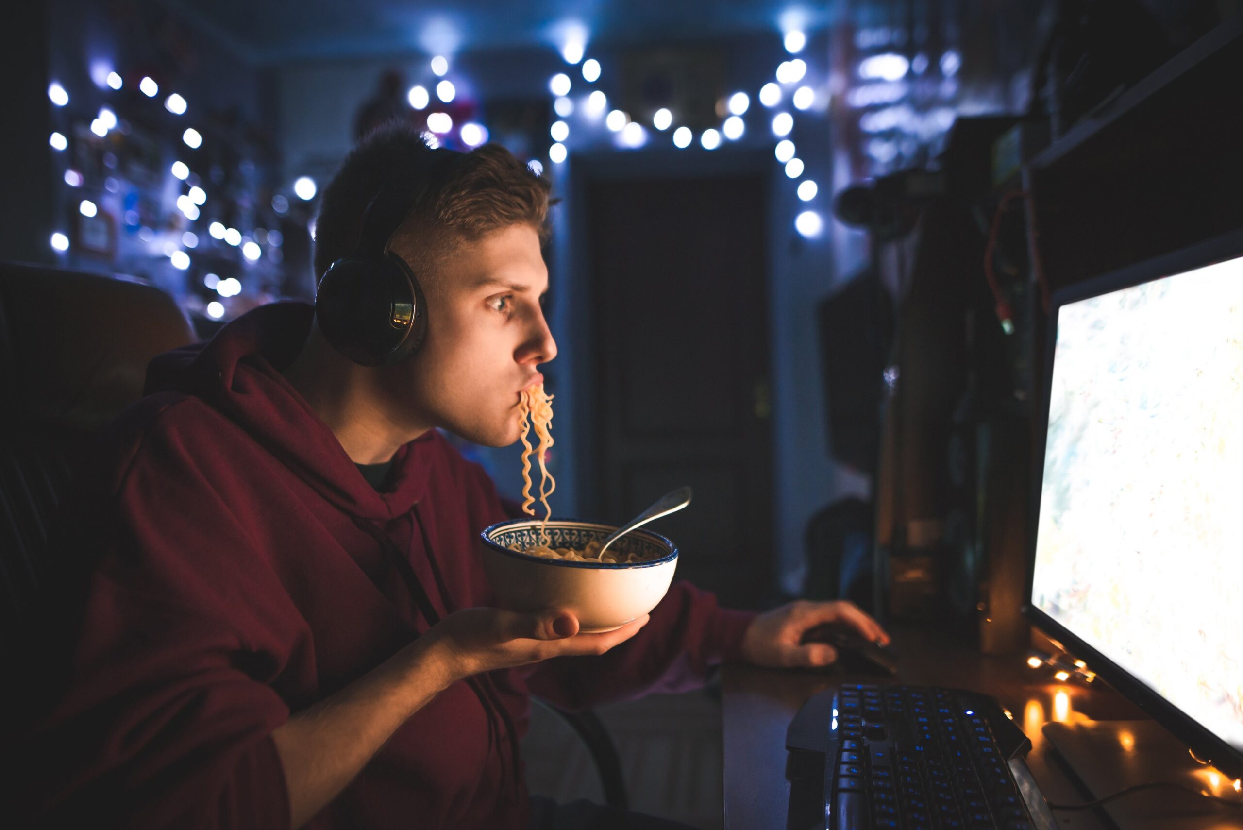 a man in a red hoodie eating noodles while playing video games